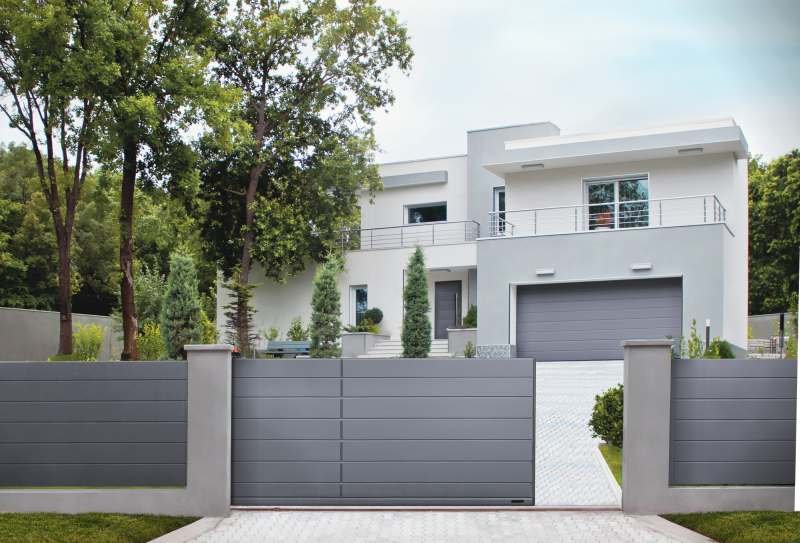 Nowoczesną bryłę domu podkreśla brama garażowa z dopasowanymi kolorystycznie drzwiami wejściowymi oraz ogrodzeniem