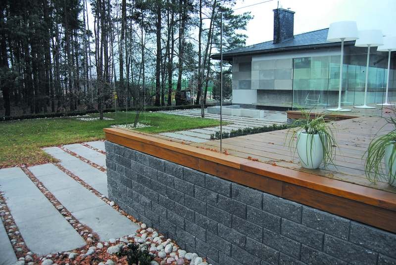 Betonowy murek oraz oryginalna w formie donica z betonowych elementów współgrają z architekturą budynków i wpisują się w otoczenie