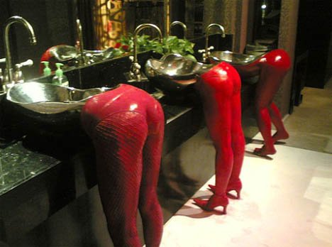 Czerwone, damskie nogi całkowicie odwracają uwagę od nietypowych umywalek - stalowych, w nieregularnych kształtach